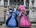 Two beautiful women holding fans and wearing hand painted masks and ornate blue and pink costumes at Venice Carnival Royalty Free Stock Photo