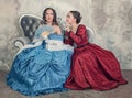 Two beautiful women in medieval dresses gossip on the sofa Royalty Free Stock Photo