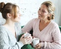 Two beautiful women- mother and daughter sitting on the sofa at home. They drink coffee, tea.