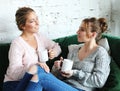 Two beautiful women- mother and daughter sitting on the sofa at home. They drink coffee, tea.