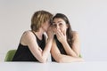 Two beautiful women over white background. The blonde girl is telling a secret on the ear to her brunette friend and she is Royalty Free Stock Photo