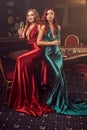 Two beautiful women are posing against a poker table in luxury casino.