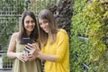 Two beautiful women taking selfie with mobile phone. green background. One is holding a cup of coffee. They are laughing and Royalty Free Stock Photo