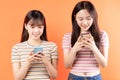 Two beautiful young asian girls are using mobile phones on orange background