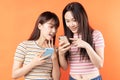 Two beautiful young asian girls are using mobile phones on orange background