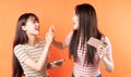 Two beautiful young asian girls are using mobile phones on orange background