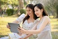 Two beautiful young Asian women are using tablet, taking selfies while picnic in the park Royalty Free Stock Photo