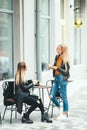 Two beautiful young blonde girls drinking coffee and talking near the cafe Royalty Free Stock Photo