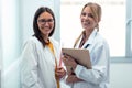 Two beautiful young female doctor holding digital tablet while smiling looking at camera in hospital Royalty Free Stock Photo