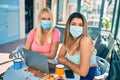 Two beautiful and young girl friends together using computer laptop at cafeteria wearing covid-19 safety mask Royalty Free Stock Photo