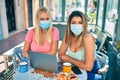 Two beautiful and young girl friends together using computer laptop at cafeteria wearing covid-19 safety mask Royalty Free Stock Photo