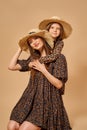 Two beautiful young girls sisters in nice animal pattern dresses with straw hats posing in studio Royalty Free Stock Photo