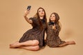 Two beautiful young girls sisters take selfies in nice animal pattern dresses with straw hats posing in studio Royalty Free Stock Photo