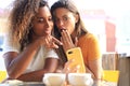 Two beautiful young woman sitting at cafe drinking coffee and looking at mobile phone Royalty Free Stock Photo