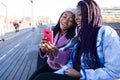 Two beautiful young woman using mobile phone in the street. Royalty Free Stock Photo