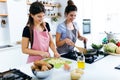 Two beautiful young women cooking chards and slicing potatoes in the kitchen. Royalty Free Stock Photo