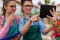 Two beautiful young women entrepreneurs in flower greenhouse using tablet for their business