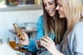 Two beautiful young women friends eating burgers while looking smart phone in the restaurant Royalty Free Stock Photo