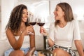 Two beautiful young women, Hispanic and Caucasian, sitting on a sofa toasting with a glass of red wine - Multiethnic happy female Royalty Free Stock Photo