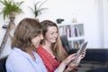 Two beautiful young women at home sitting on sofa or settee using a tablet PC computer and smiling Royalty Free Stock Photo