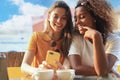 Two beautiful young woman sitting at cafe drinking coffee and looking at mobile phone. Royalty Free Stock Photo