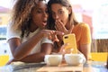 Two beautiful young woman sitting at cafe drinking coffee and looking at mobile phone Royalty Free Stock Photo