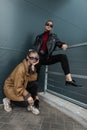 Two beautiful young women in trendy denim clothes with a leather jacket in sunglasses posing near a metal wall outdoors Royalty Free Stock Photo