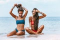 Two beautiful young women twin sisters in bikini sitting on sand on the beach at sunny day Royalty Free Stock Photo