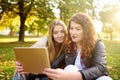 Two beautiful young women using tablet computer together at sunny park. Remote communication. Dating site