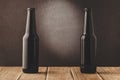 two beer bottles on a wooden table against a dark background/black bottles of beer against a dark background with this light, cop Royalty Free Stock Photo