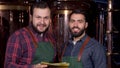 Two beer makers smiling to the camera, while working at their brewery