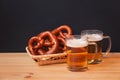 Two beer mugs and basket with soft pretzels on wooden table on dark background. Selective focus Royalty Free Stock Photo