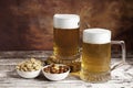 Two beer mugs with foam and bowls of peanuts and almonds Royalty Free Stock Photo