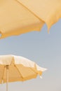 Two beige cotton beach umbrellas against a blue sky