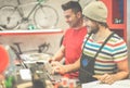 Two bicycle repairer colleagues working in bike garage - Positive mood bmx seller using computer in workshop - Retail selling and