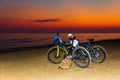 Two bicycles stand on a sandy beach by the sea at sunset