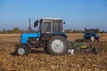 Two big blue tractor plowing a field and remove the remains of previously mown corn.