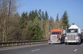 Two big rig orange and white semi trucks with tank semi trailer transporting liquid on the wide road in sunny day Royalty Free Stock Photo