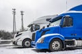 Two big rig semi trucks with high cabs standing in row on the winter truck stop parking lot covered with snow and ice Royalty Free Stock Photo