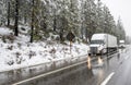Two big rig semi trucks with semi trailers standing on the wet highway road shoulder waiting for the end of the winter snowing Royalty Free Stock Photo