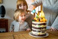 Two big sisters lighting a candle on their toddlers brother birthday cake. Cutting homemade birthday cake. Celebrating second Royalty Free Stock Photo