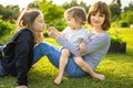 Two big sisters and their toddler brother having fun outdoors. Two young girls holding baby boy on summer day. Children with large Royalty Free Stock Photo