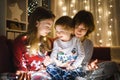 Two big sisters and their toddler brother playing with Christmas lights in a cozy living room on Christmas eve. Kids spending time Royalty Free Stock Photo