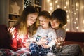 Two big sisters and their toddler brother playing with Christmas lights in a cozy living room on Christmas eve. Kids spending time Royalty Free Stock Photo