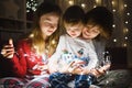 Two big sisters and their toddler brother playing with Christmas lights in a cozy living room on Christmas eve. Kids spending time Royalty Free Stock Photo