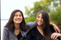 Two smiling biracial teen girls smiling outdoors by lake, huggi