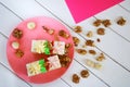 Two biscuit cakes with cream decorations are lying in a plate, next to sprinkled macadamia and walnuts on a white and pink Royalty Free Stock Photo