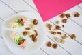 Two biscuit cakes with cream decorations are lying in a plate, next to sprinkled macadamia and walnuts on a white and pink Royalty Free Stock Photo