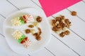 Two biscuit cakes with cream decorations, macadamia nuts and walnuts in a plate on a white and pink background. Wooden table and Royalty Free Stock Photo