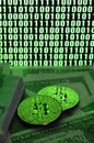 Two bitcoins lies on a pile of dollar bills on the background of a monitor depicting a binary code of bright green zeros and one u Royalty Free Stock Photo